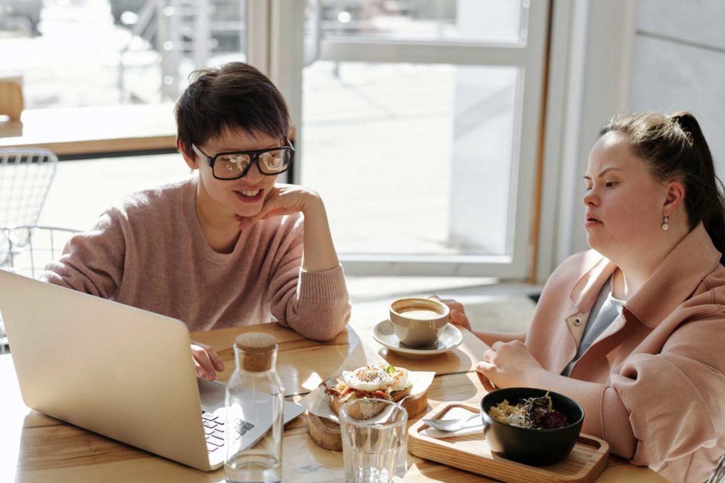 Two young women with disabilities sitting down at a cafe having a business meeting.