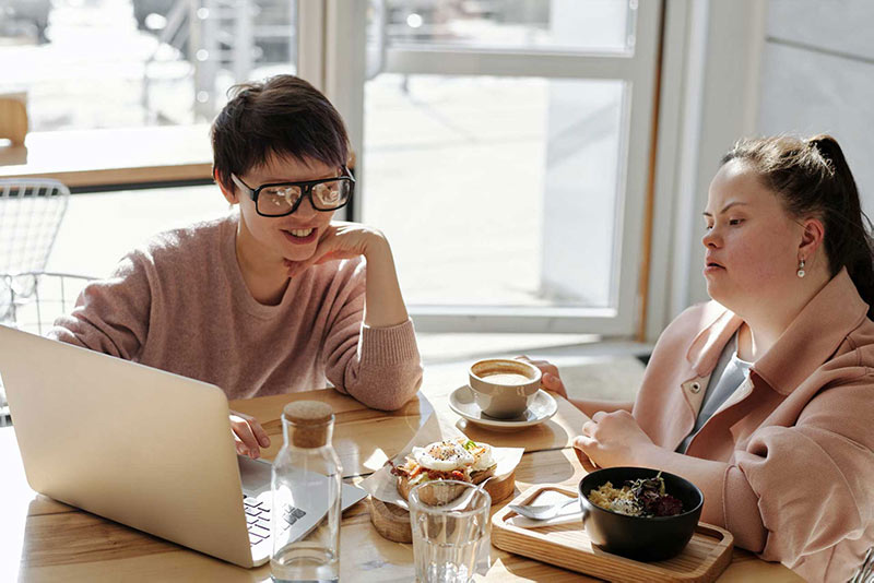 Two women younger women with disabilities talking over lunch looking at a computer