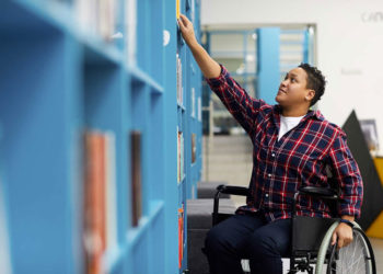 An individual in a wheel chair reaching for a book at a library