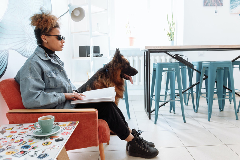 Visually Impaired Woman reading braille with Seeing Eye dog next to her sitting down