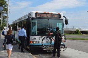 HRT Bus pulled to the curb with a person putting a bike on the front of the bus and a person getting on the bus.