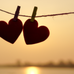 Two cardboard heart-shaped cut-outs are clothes pinned to a rope. The sun sets in the background.