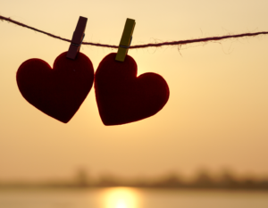 Two cardboard heart-shaped cut-outs are clothes pinned to a rope. The sun sets in the background.