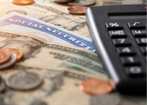 close up shot of dollar bills, coins, a calculator, and the top of a Social Security card.
