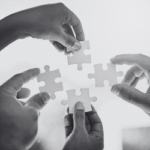 Four hands hold puzzle pieces in a circle shape